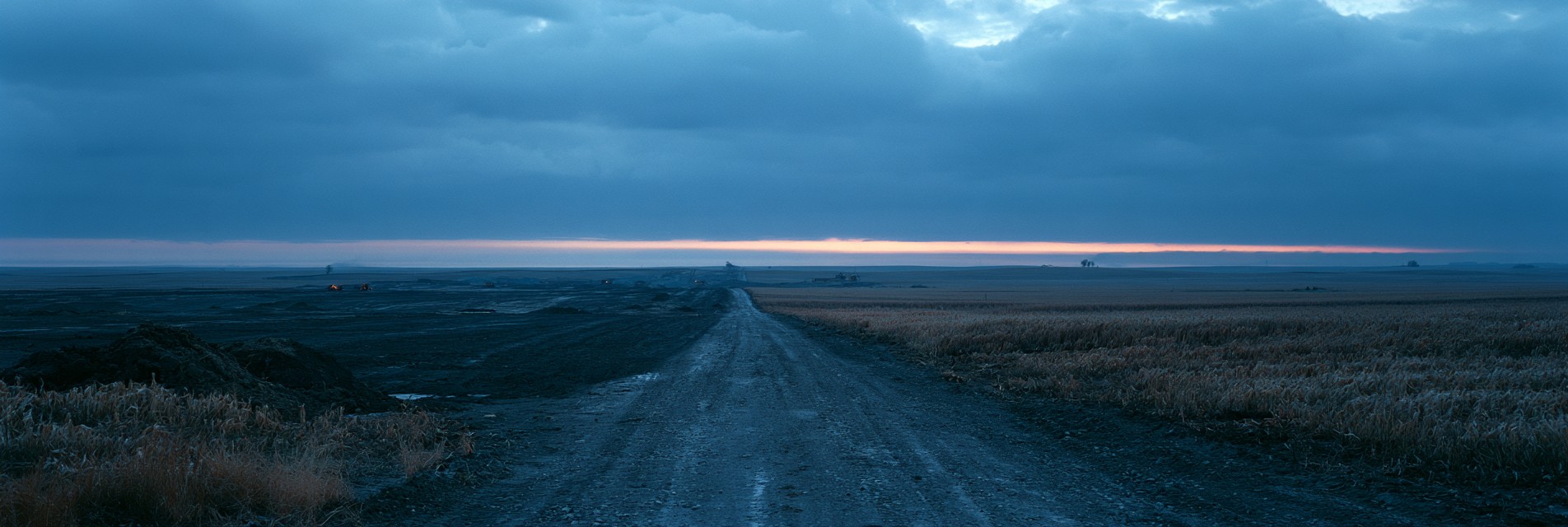 Early-stage construction on flat open farmland at dusk, graded earth and gravel access roads